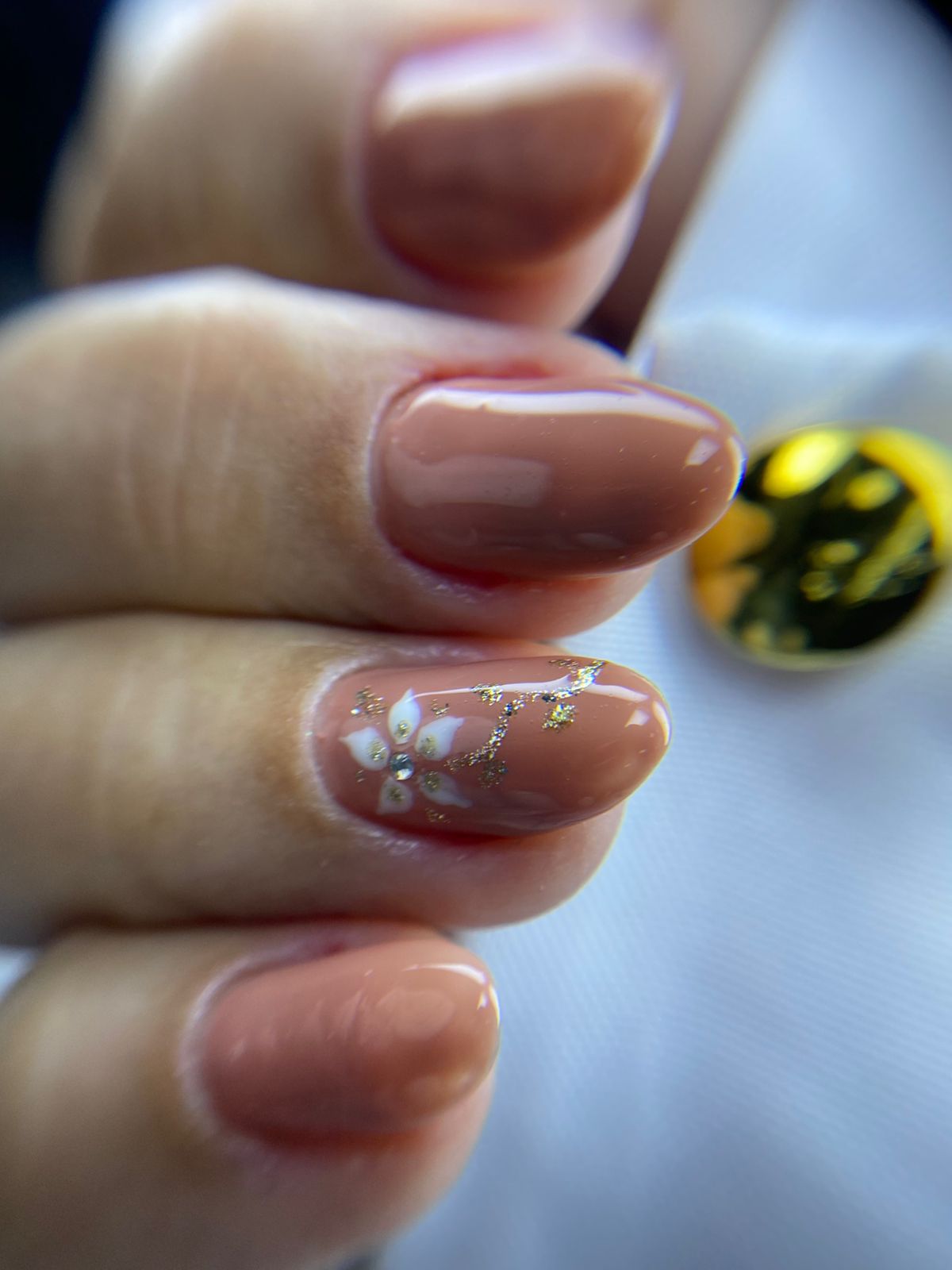 Unhas nude com flor delicada e glitter dourado feitas no Millano